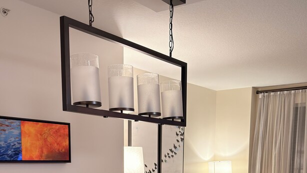 Een moderne woonkamer met een eettafel met glazen blad, gestoffeerde stoelen, een bank en een hanglamp.