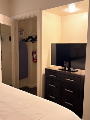 A hotel room with a bed, a TV on a dresser, a closet with clothes and a fire extinguisher. - King Villa Resort with Balcony near Orlando’s I-Drive (Orlando)