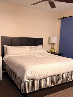 A neatly made bed with a striped bed skirt, a bedside lamp, and a ceiling fan. - King Villa Resort with Balcony near Orlando’s I-Drive (Orlando)