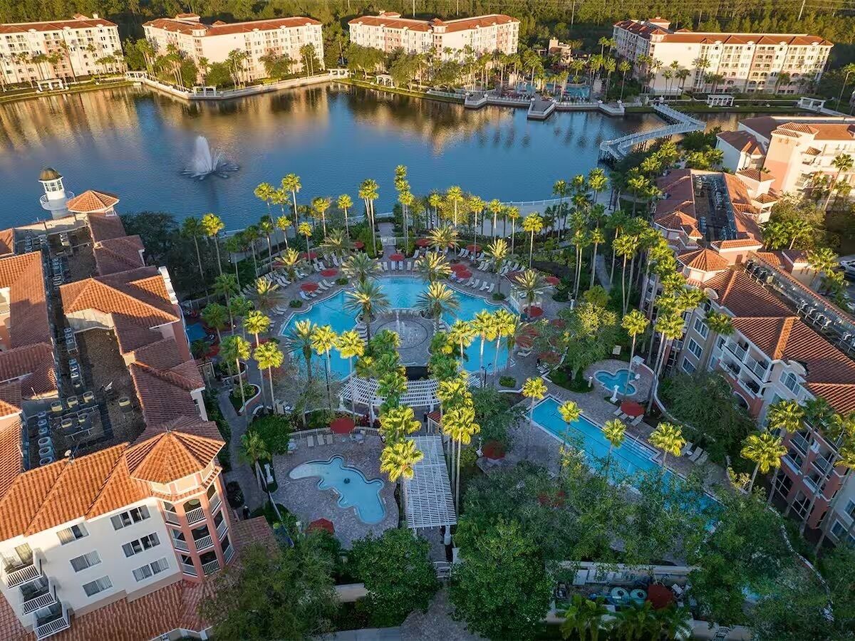 Un resort con varias piscinas, palmeras y una masa de agua.