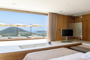 Ein modernes Hotelzimmer mit einem großen Bett, einem Fernseher und einem Balkon mit Sitzgelegenheit und Meerblick.