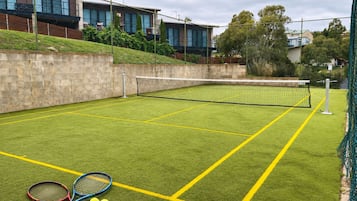 An outdoor tennis court with a net, two tennis rackets, and three tennis balls.