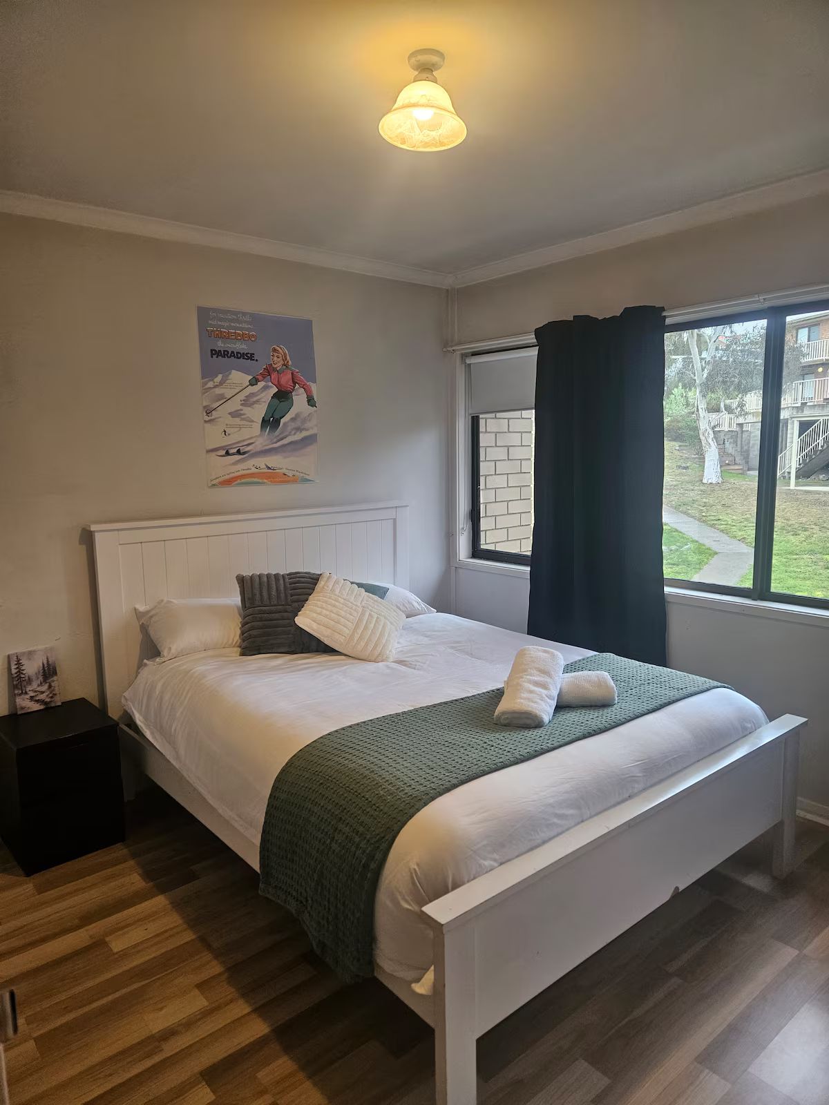 A bedroom with a bed, a nightstand, a window with curtains, and a poster on the wall.