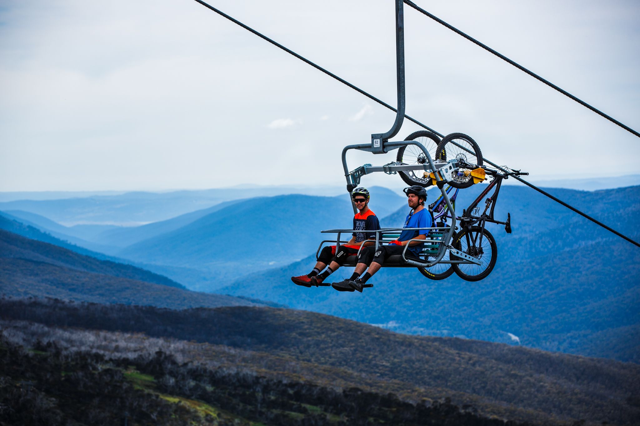 A cable car with two passengers and bicycles, set against a mountainous backdrop.