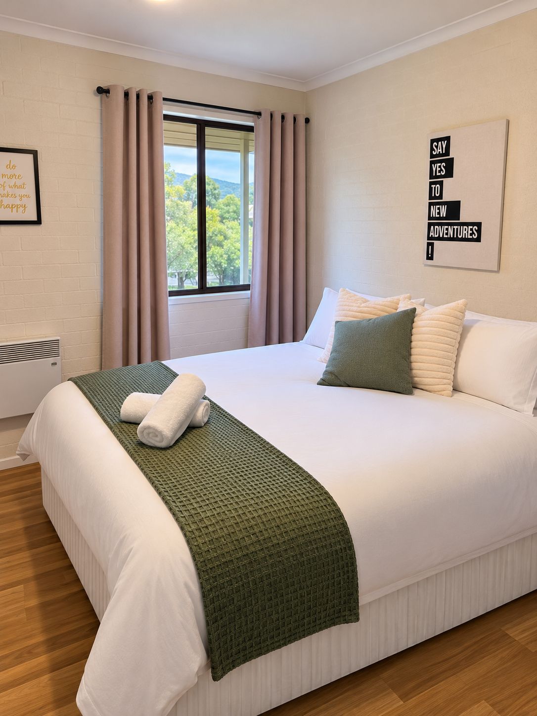 A neatly made bed with a green throw blanket and pillows, a window with curtains, and a motivational quote on the wall.