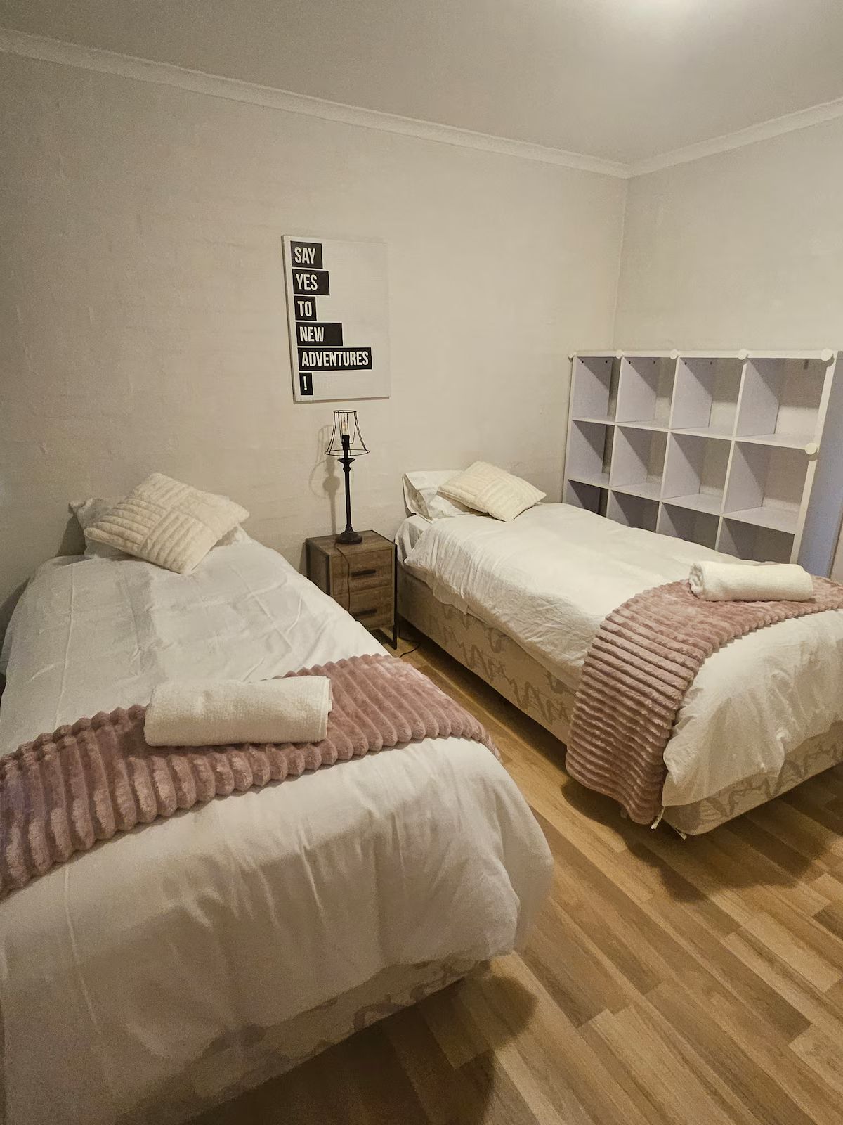 A bedroom with two beds, a nightstand, a lamp, and a wall sign.