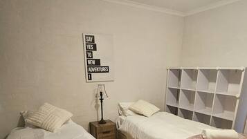 A bedroom with two beds, a nightstand, a lamp, and a wall sign.