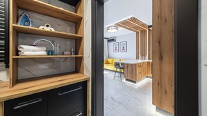 Um banheiro moderno com toucador de madeira, prateleiras de mármore e um sofá amarelo ao fundo.