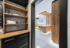 A modern bathroom with a wooden vanity, marble shelves, and a yellow sofa in the background. - Podwisłocze Riverside Apartment (Rzeszów)