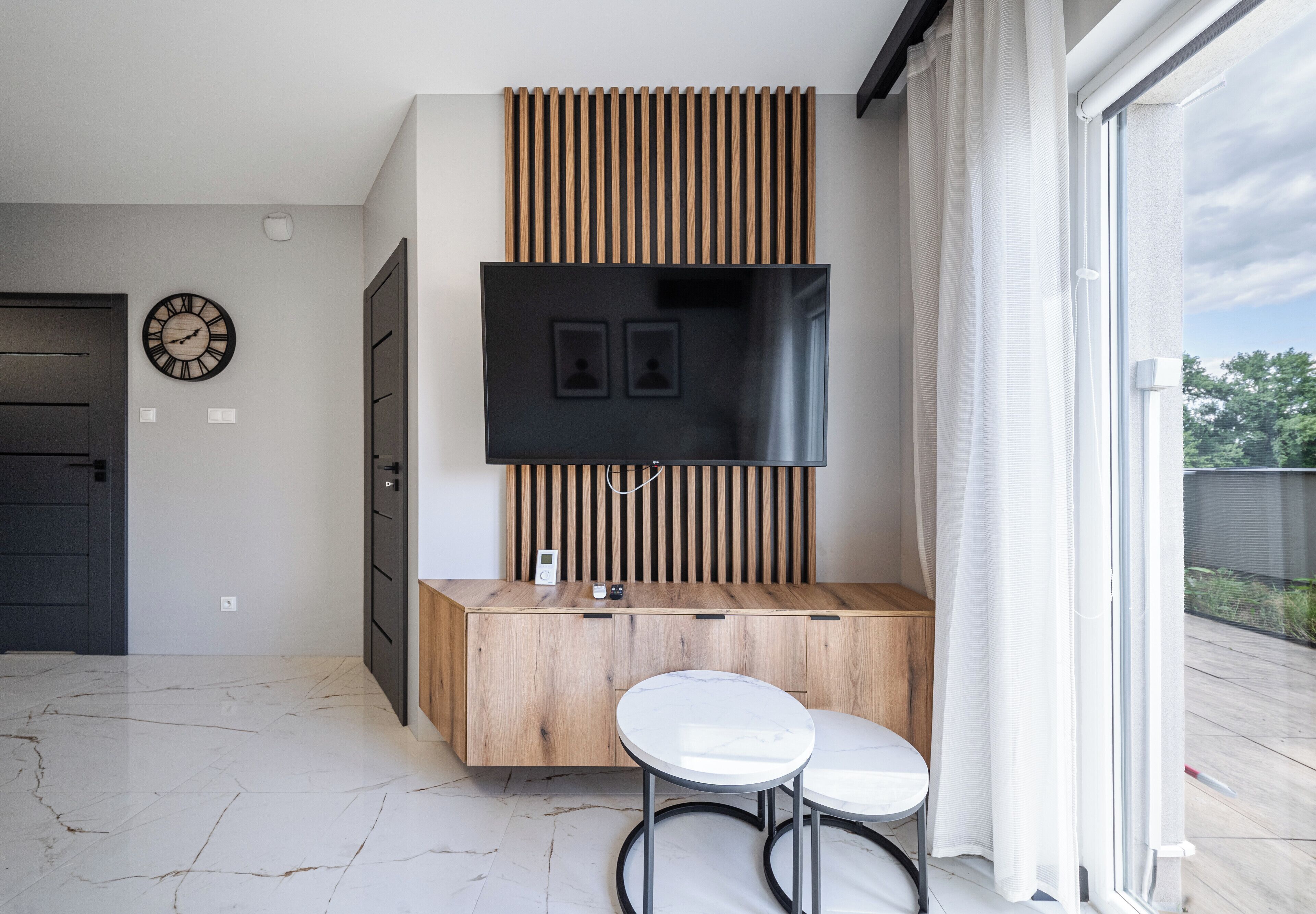 Una sala de estar moderna con un televisor de pantalla plana montado en un panel de madera, un armario empotrado y una pequeña mesa redonda.