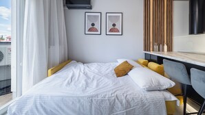 Quarto de hotel com cama, escrivaninha, duas obras de arte emolduradas e janela com cortinas.