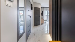 Um corredor com piso de mármore, um relógio e uma porta que dá para outro quarto.