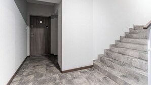 Um corredor com uma porta de madeira marcada com o número 47, que dá para uma escadaria com degraus de pedra cinzenta.