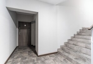 A hallway with a wooden door marked with the number 47, leading to a staircase with grey stone steps. - Podwisłocze Riverside Apartment (Rzeszów)