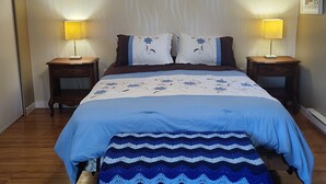Quarto com cama, duas mesas de cabeceira com abajures, parede com padrão ondulado e quadro na parede.