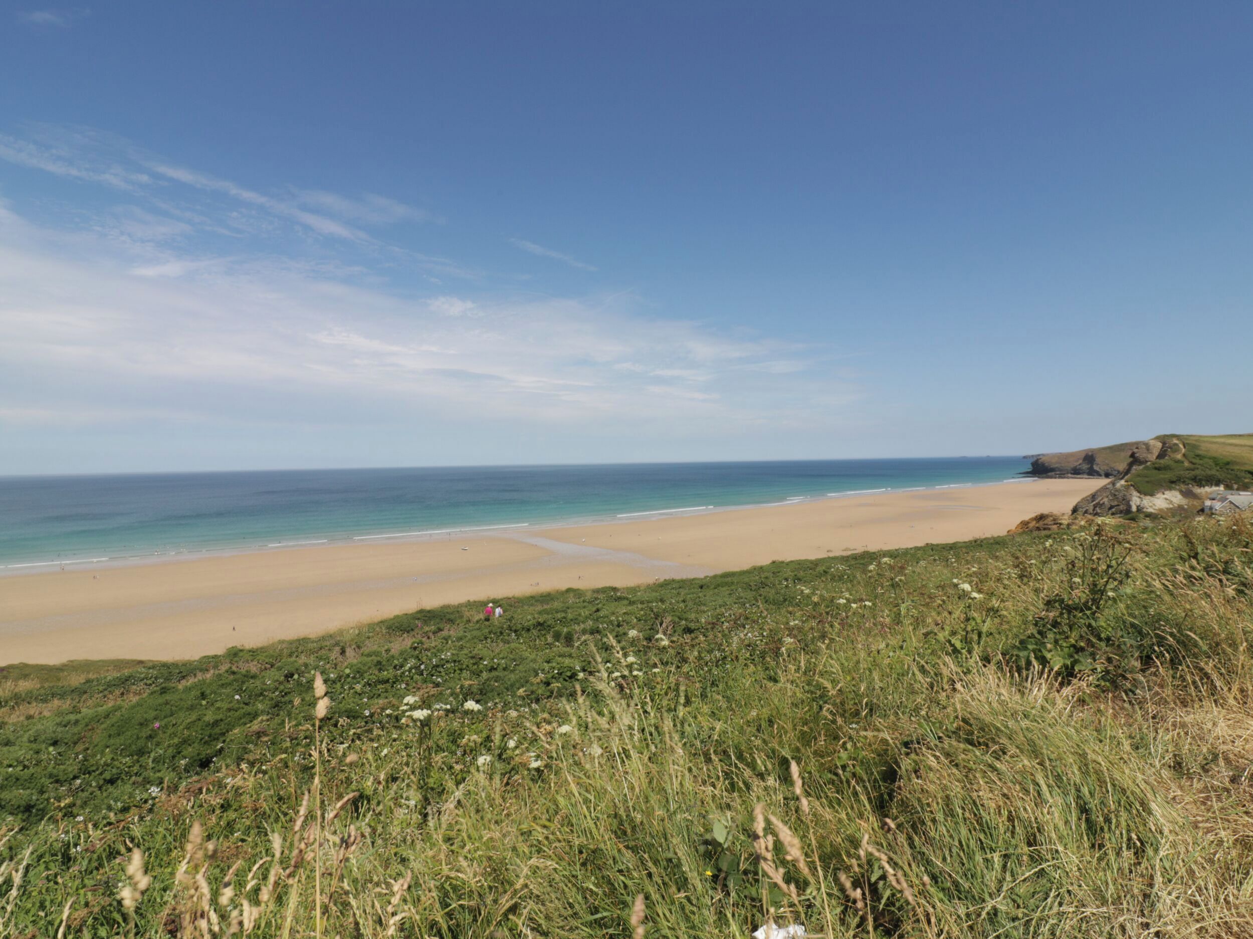 A coastal landscape with a sandy beach, grassy areas, and a clear blue sky.