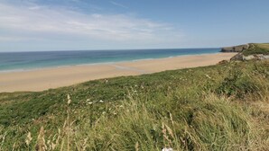 A coastal landscape with a sandy beach, grassy areas, and a clear blue sky. - 1 GRENVILLE ROAD, pet friendly, country holiday cottage in Truro (Truro)