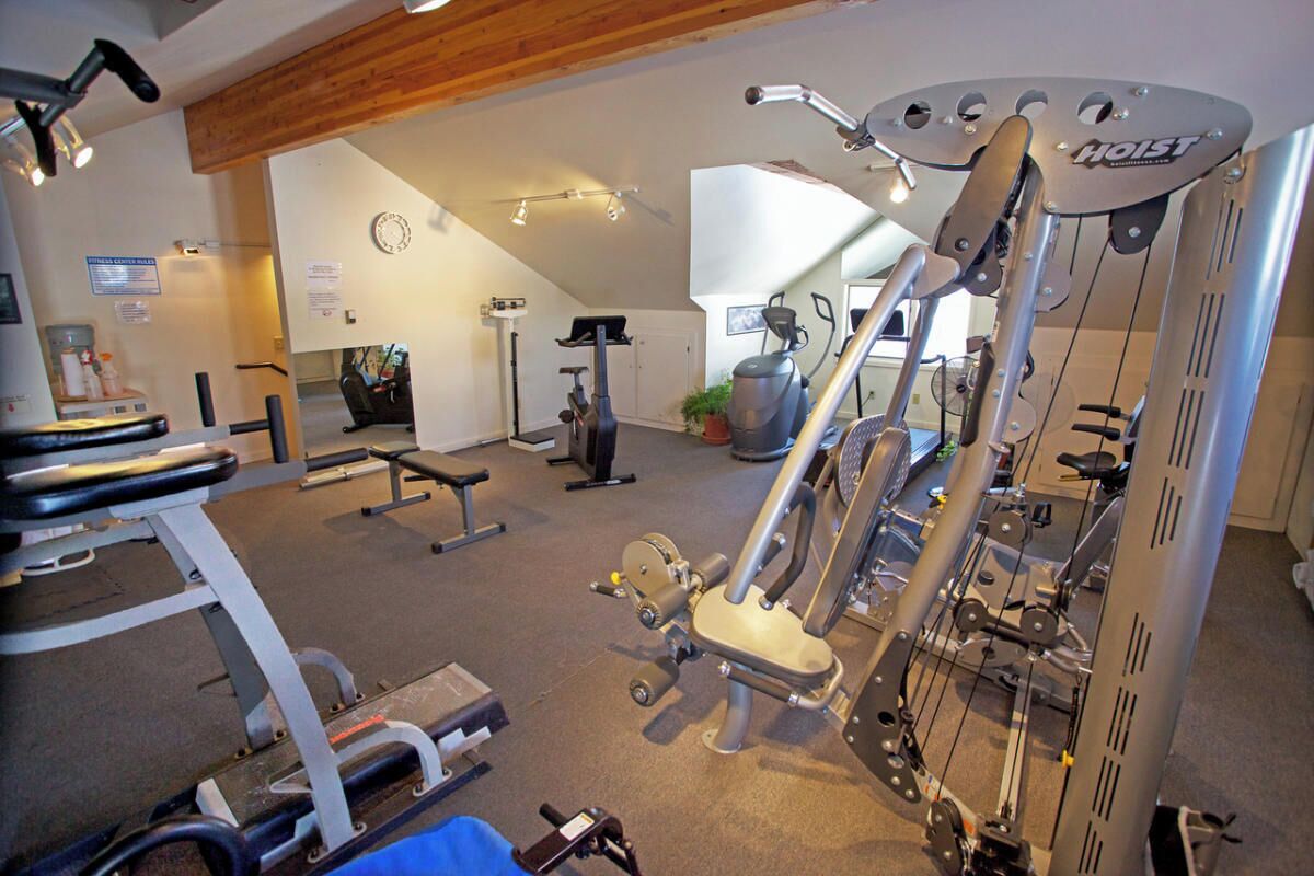 A gym with various exercise equipment, including a rowing machine, a bench press, and a stationary bike.