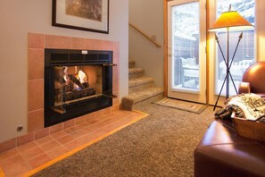 A fireplace with a fire, a staircase, and a floor lamp. - Private 2-bedroom luxury cabin in Estes Park with cozy charm (Estes Park)