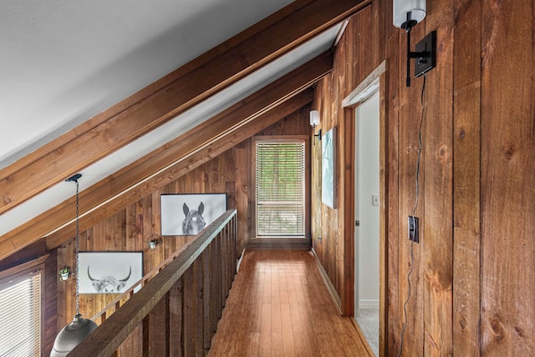 A wooden interior with a sloped ceiling, a staircase, and framed pictures on the walls.