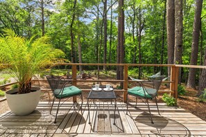 A wooden deck with two tables and chairs, surrounded by a forest.