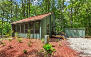 A wooden cabin with a porch, surrounded by a forest.