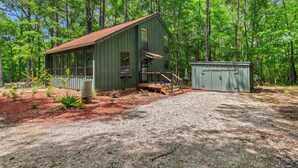 A rustic cabin with a wooden deck and a gravel driveway.
