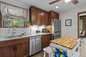 A kitchen with wooden cabinets, a stainless steel refrigerator, a dishwasher, and a wooden dining table.