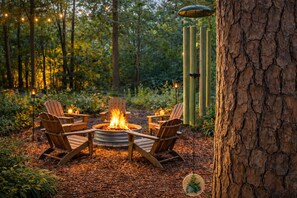 A circular fire pit with seating around it, set in a forested area with trees and a wooden structure nearby. - Jackson’s Urban Cabin Escape (Jackson)