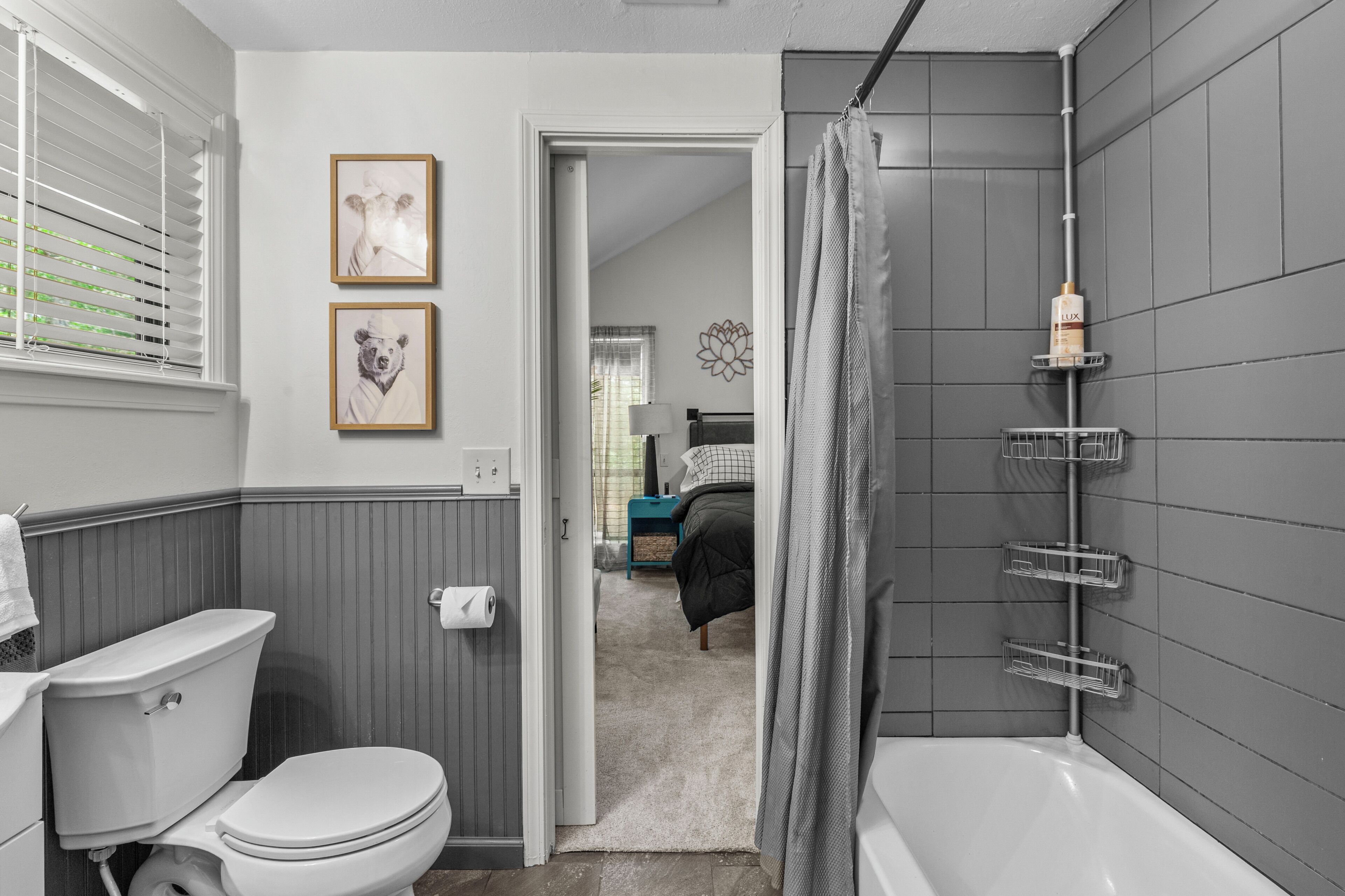 A bathroom with a toilet, a bathtub, and a shower curtain. There are framed pictures on the wall and a towel rack.