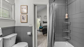 A bathroom with a toilet, a bathtub, and a shower curtain. There are framed pictures on the wall and a towel rack.
