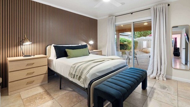 Une chambre à coucher avec un lit, des tables de chevet, un bureau, un miroir et une vue sur l’extérieur.