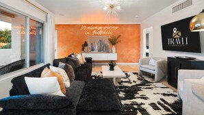 Un salon moderne avec un canapé noir, des fauteuils blancs et un tapis en peau de vache. Un panneau néon affiche l'inscription : « Il fait toujours beau à Scottsdale. »