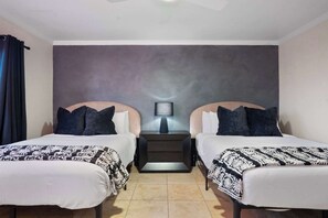 A hotel room with two beds, a nightstand with a lamp, and a plain wall. - NEW|Iconic Granada Grotto|Pool & Hottub| Sleeps 12 (Scottsdale)