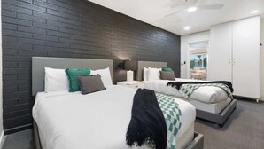 Une chambre d’hôtel avec deux lits, un mur en briques sombres, un ventilateur de plafond et une vue sur l’extérieur.