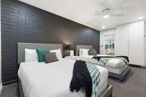 A hotel room with two beds, a dark brick wall, a ceiling fan, and a view of the outdoors. - NEW|Iconic Granada Grotto|Pool & Hottub| Sleeps 12 (Scottsdale)