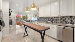 Une cuisine moderne avec des meubles blancs, un lave-vaisselle Bosch et un coin repas comprenant une table en bois et des chaises suspendues.