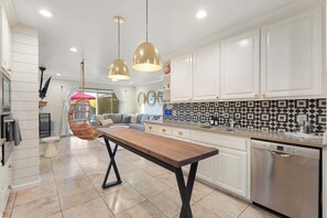 A modern kitchen with white cabinets, a Bosch dishwasher, and a dining area with a wooden table and hanging chairs. - NEW|Iconic Granada Grotto|Pool & Hottub| Sleeps 12 (Scottsdale)