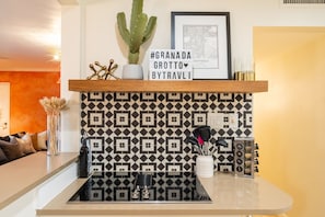 A kitchen with a black and white patterned backsplash, a cactus on the counter, and a sign with #GRANADA GROTTO BYTRAVLI. - NEW|Iconic Granada Grotto|Pool & Hottub| Sleeps 12 (Scottsdale)