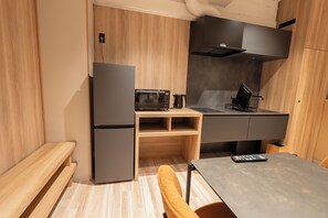A compact kitchenette with a refrigerator, microwave, and stove, a small wooden table, and a chair. - Villa Customa (Taito City)