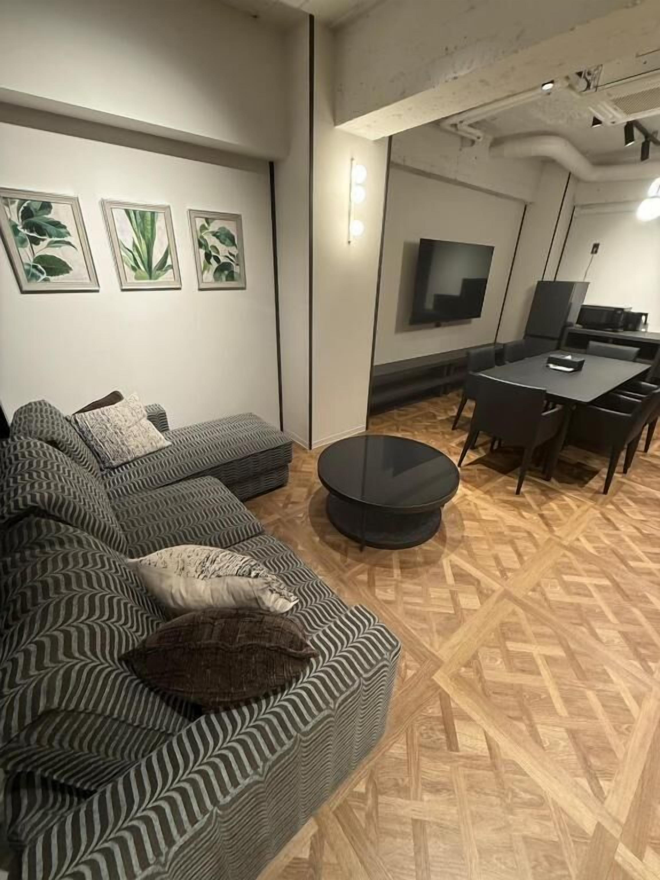 A modern living room with a sofa, a round coffee table, and a flat-screen TV mounted on the wall.