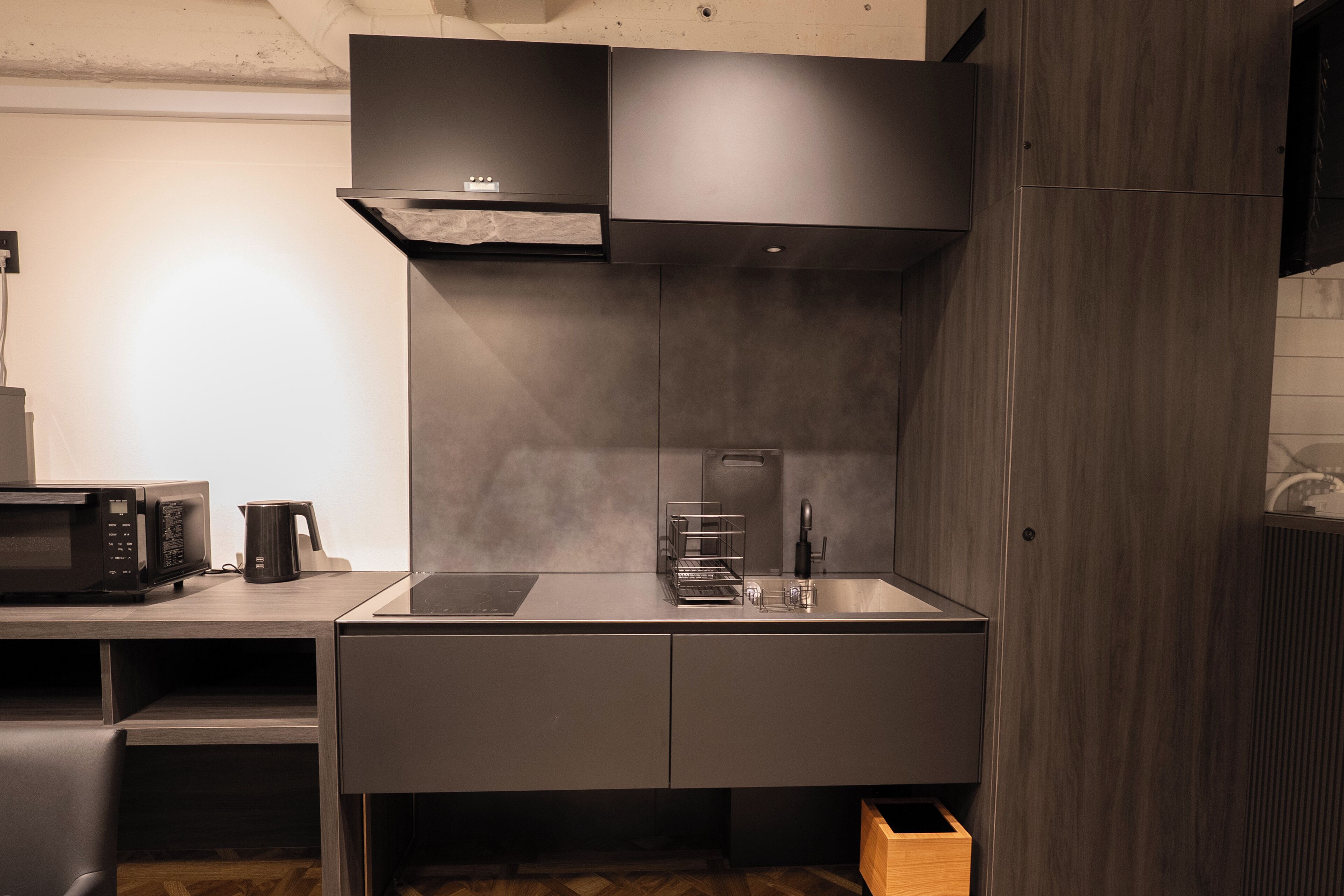 A modern kitchen with a built-in microwave, kettle, and a stainless steel sink.