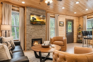 A cozy living room with a fireplace, leather furniture, and a stone wall. - Casa Amore - Stunning Views, Cozy Nights & Lasting Family Memories (Gatlinburg)