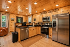 A modern kitchen with wooden cabinetry, stainless steel appliances, and a central island. - Casa Amore - Stunning Views, Cozy Nights & Lasting Family Memories (Gatlinburg)