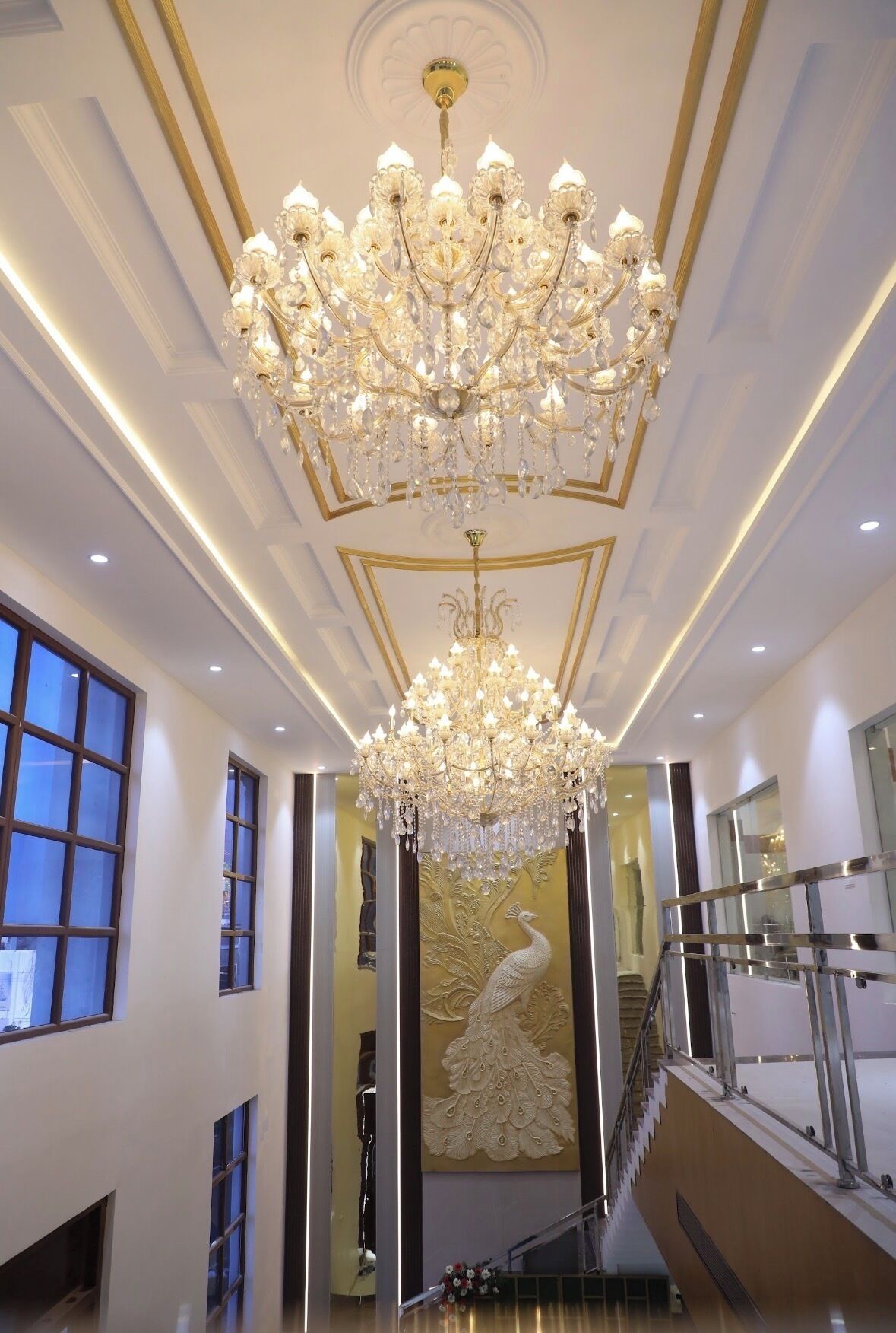 A grand interior with a large chandelier, a peacock mural, and a staircase.
