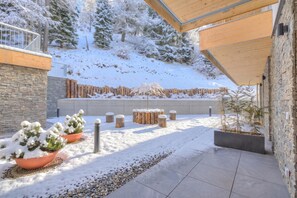 Ein verschneiter Außenbereich mit Steinmauer, Holzterrasse und Kübelpflanzen.