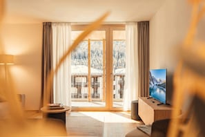 Una sala de estar moderna con un televisor grande, un sofá, una mesa de centro y vistas a un paisaje nevado a través de puertas de vidrio.