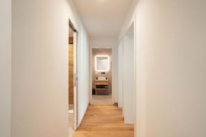 A narrow hallway with wooden flooring leading to a bathroom with a mirror and sink. - Residenza Castanea 005 San Bernardino Alpine Apartments, San Bernardino, Switzerland (San Bernardino)
