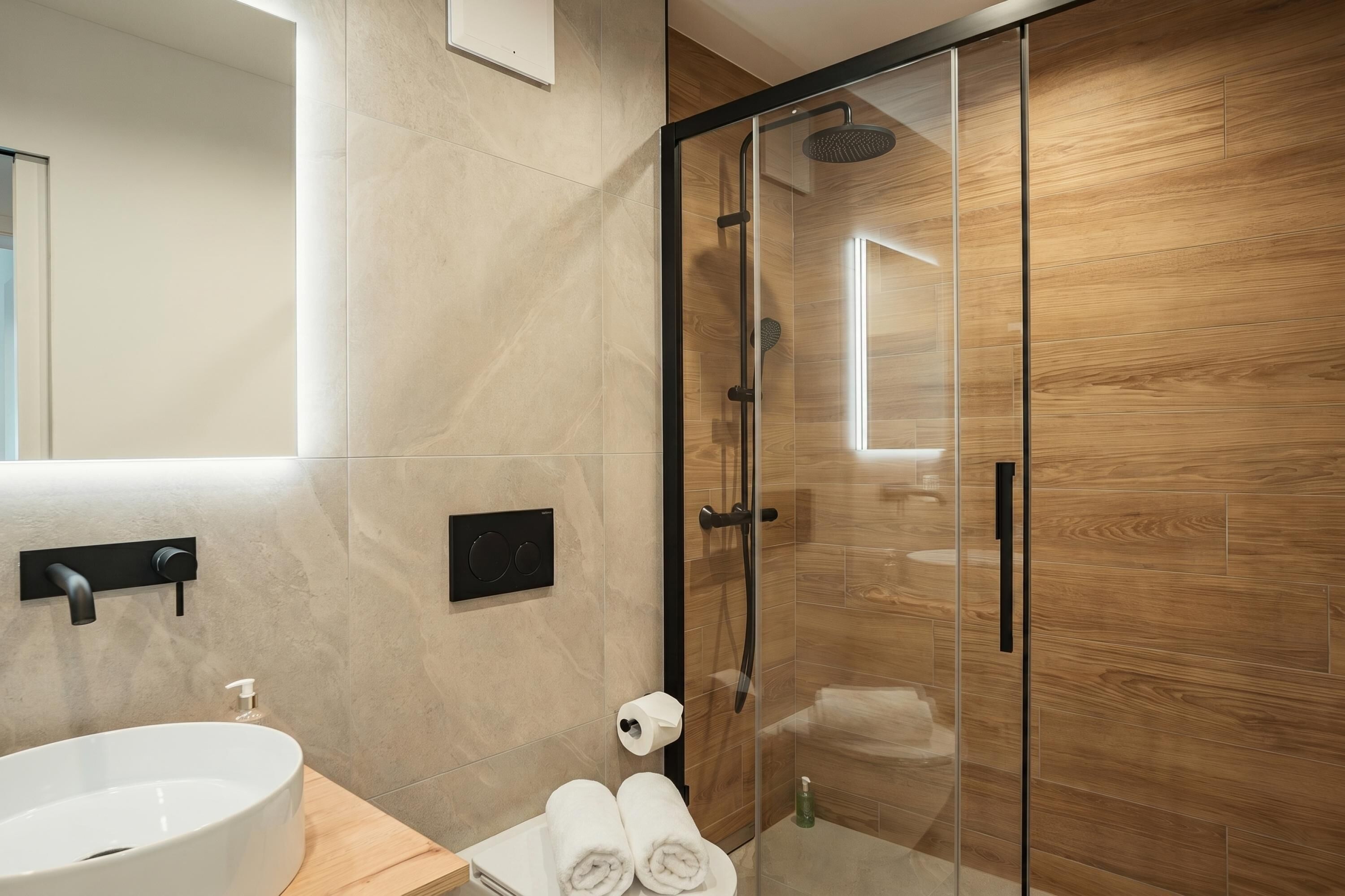 Ein modernes Badezimmer mit einer gläsernen Dusche, einem weißen Waschbecken und einer Holzkommode.