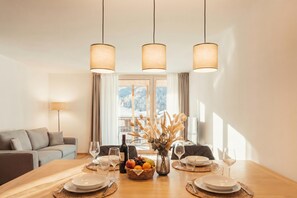 Un coin repas avec une table en bois dressée pour deux personnes, un vase contenant des fleurs séchées et une bouteille de vin.